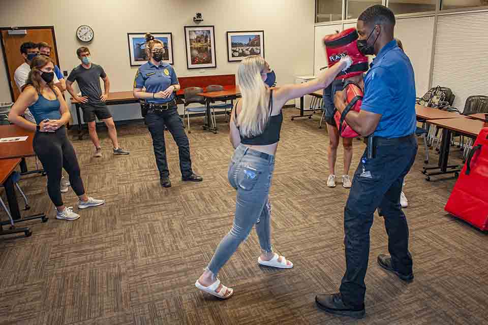 Participants stand around while one group member practices hitting a foam target.
