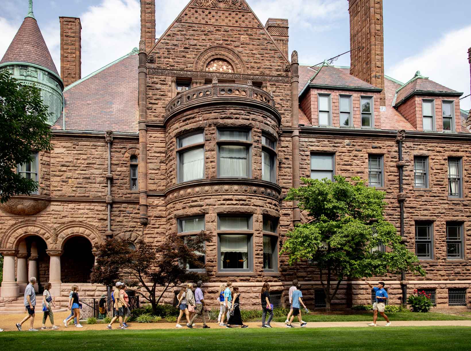 A group of people, led by a student tour guide, walks in front of a campus building.