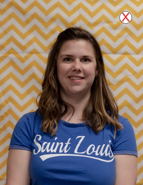 A headshot of a woman wearing a SLU t-shirt. The background of the photo is a yellow-and-white zigzag striped curtain. 
