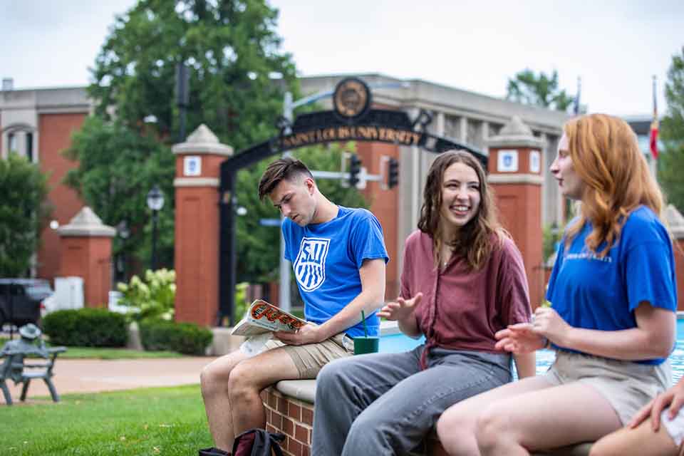 SLU students Students sit on the edge of the dolphin pond with Grand Blvd and the Saint Louis University gateway in the background on a sunny day