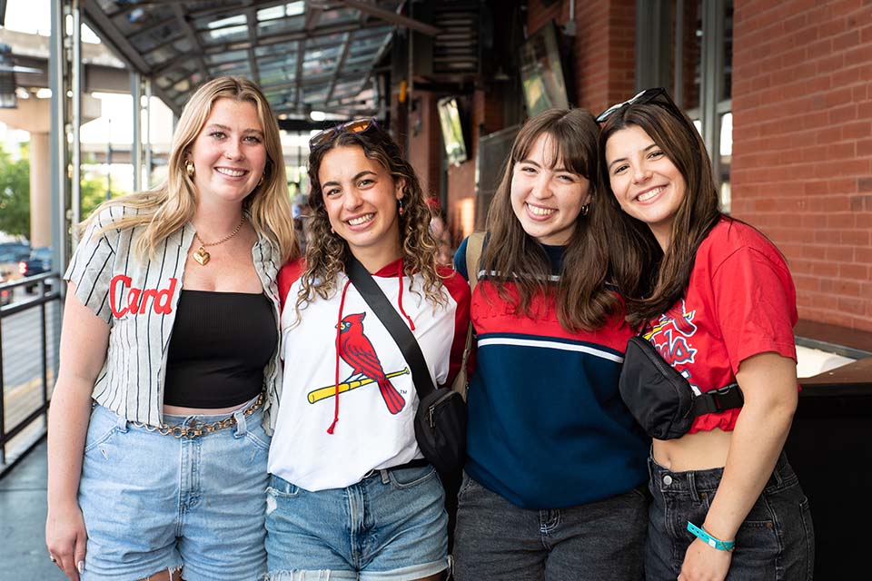 A group of students pose for a photo outside, wearing shirts that say Cardinals.
