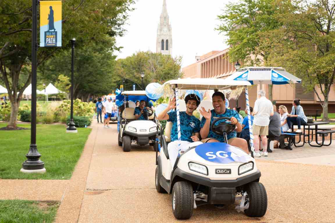 A golf cart decorated for a parade drives on SLU's campus with College Church in the background