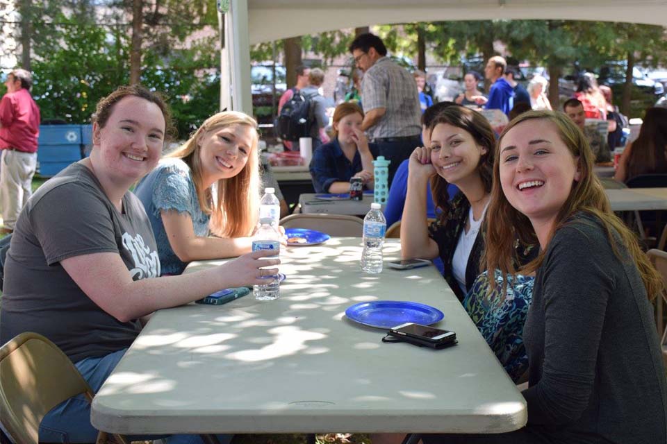 Students at a Political Science Picnic Four students sit at an outdoor table, with bottled water and paper plates in front of them.