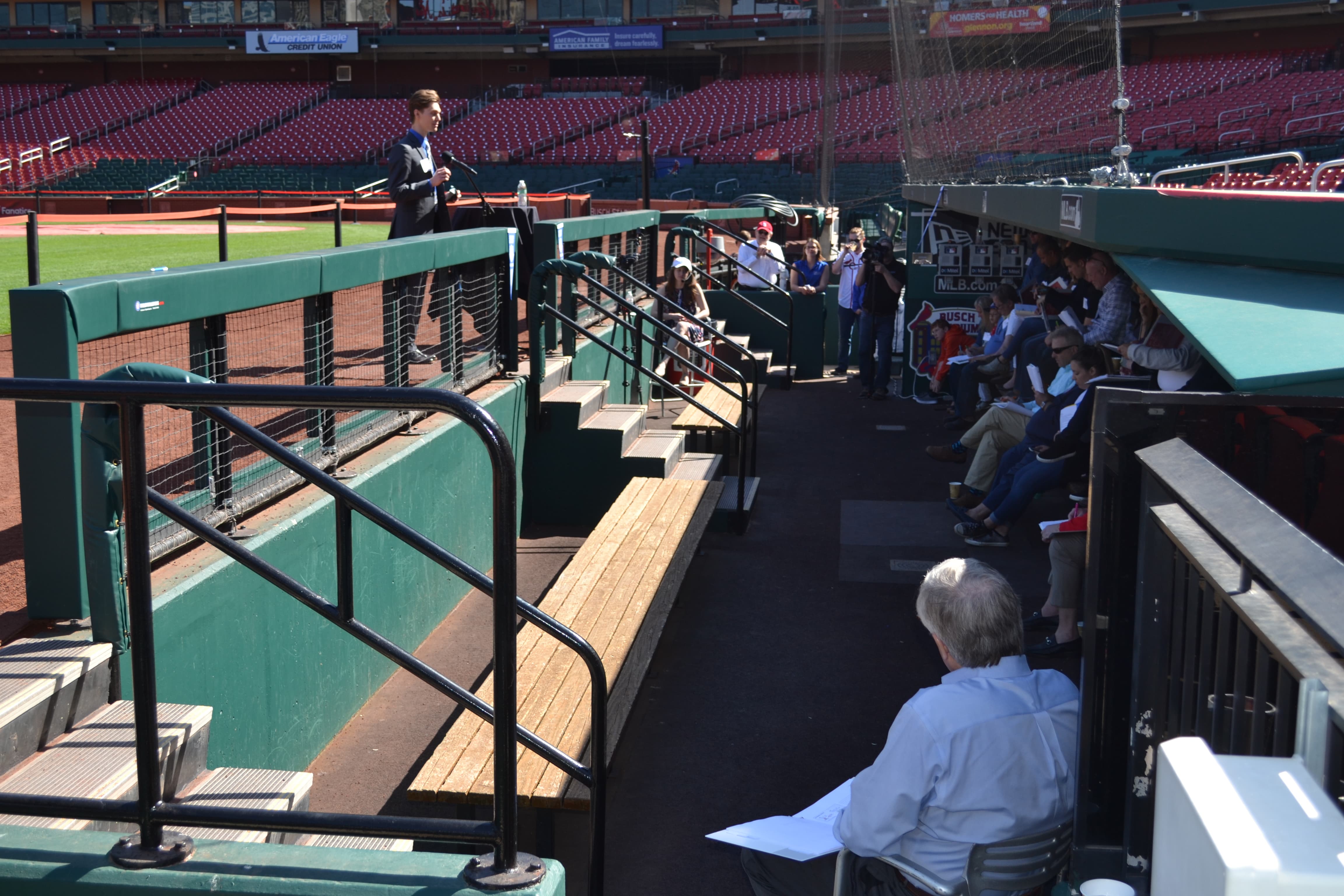 Pitch and Catch A student stands at the top of a dug out at Busch stadium speaking to a seated group