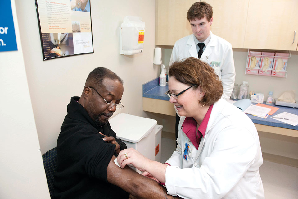 Community center. A health care worker holds something against a patient's arm while another health care worker observes.
