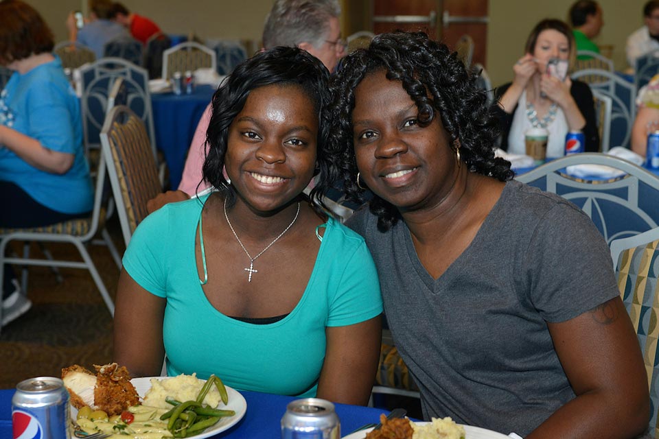 Scholarships Two students pose while sitting at a dinner with plates of food and soda cans in front of them.