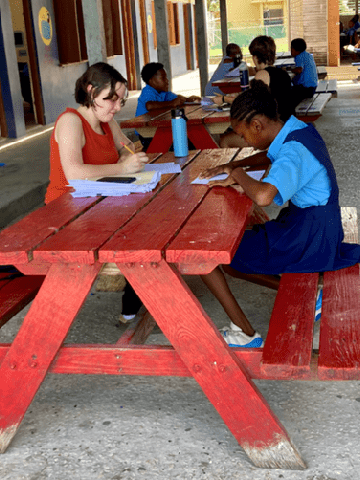 Reading Assessment A SLU student sits at a picnic table with a younger student wearing a blue school uniform while looking at school work