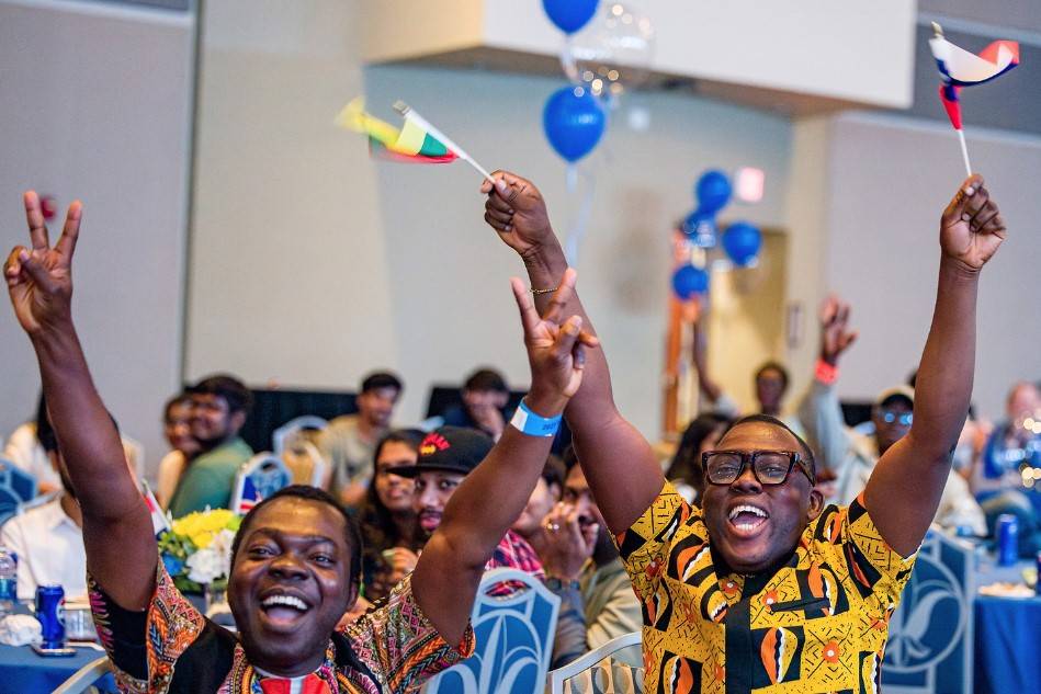 Two students raise flags and peace signs at international student orientation.