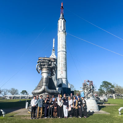Houston Trek 2025 Students standing in front of a rocket outside of the NASA building.