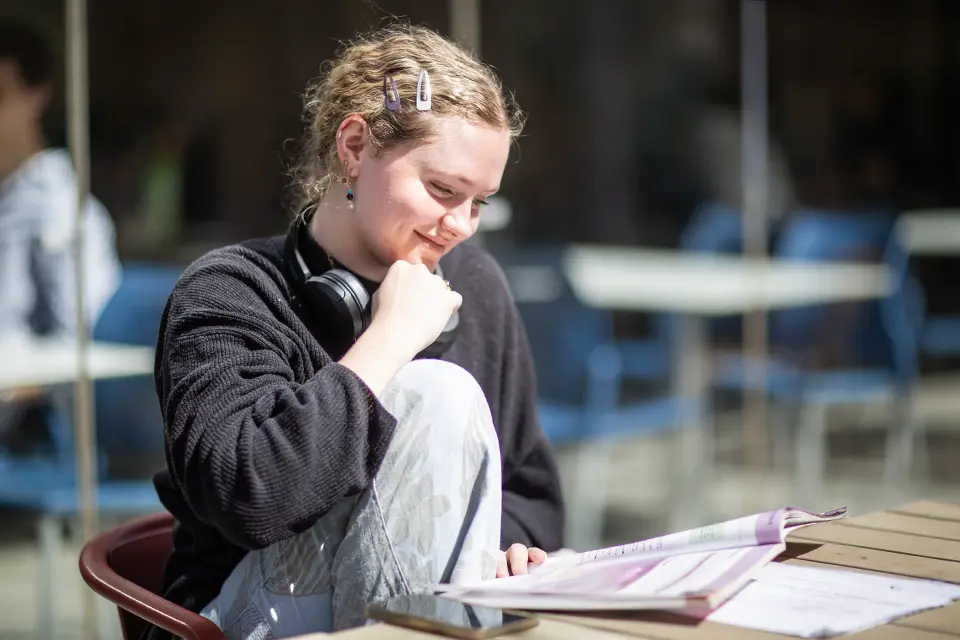 Assessments and Outcomes Student reading a book in a busy student area.