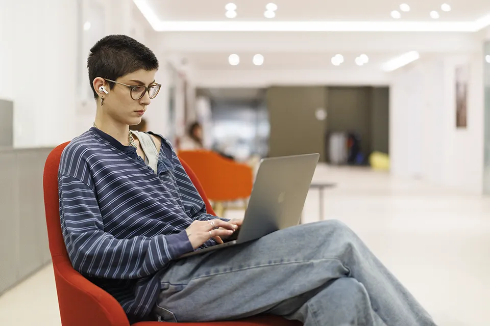 A student sitting on a chair using a laptop. A student sitting on a chair using a laptop.