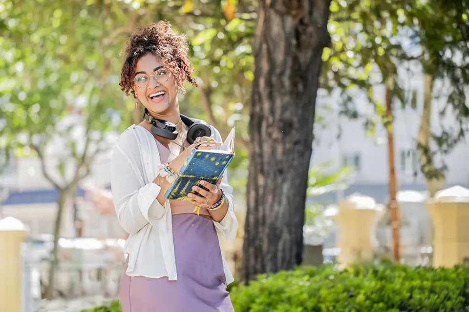 Student smiling in PRH patio. Student smiles as she holds a book in the PRH patio.