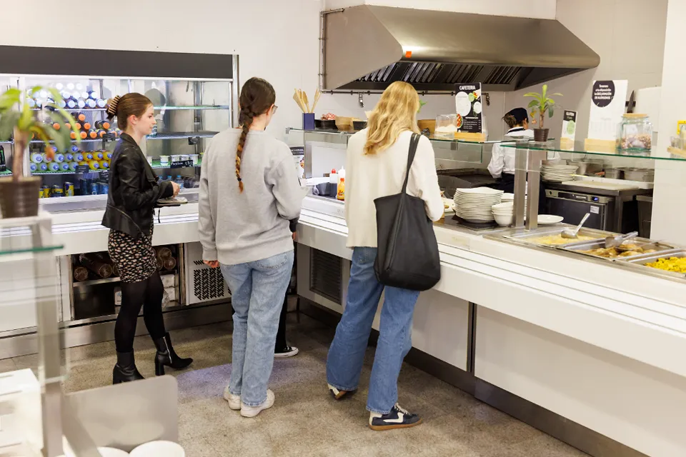 A customer selects a muffin from a selection of foods in a cafeteria.