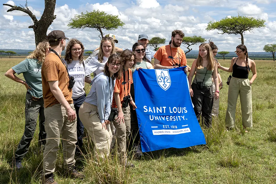 Kenya trip Landscape with a group of students in a grassy savanna, holding a SLU banner.