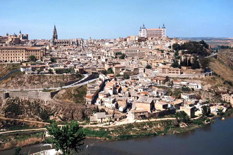 Toledo Buildings and homes in a city nestle against a hillside next to a river.