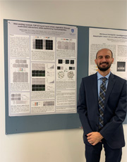 zack-grese-defense Zack Grese standing in fron of his disertation posted on a wall