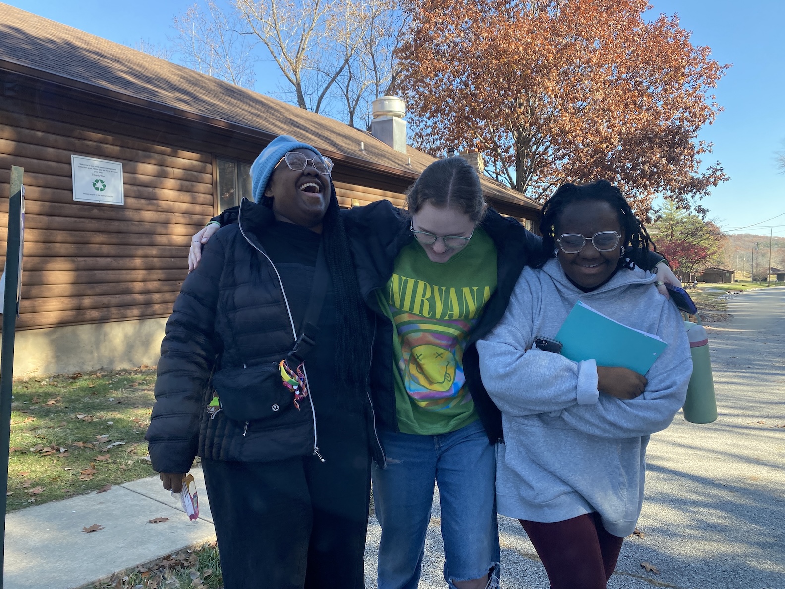 Micah Three Micah students laughing as they walk outdoors with a blue sky and a log building in the background
