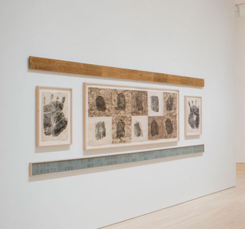 Maria Magdalena Campos-Pons, Birth Certificate, 1991. Image courtesy of the artist. An artwork by Maria Magdalena Campos-Pons titled, Birth Certificate. Multiple photographs of handprints and fingerprints are arranged on a wall.