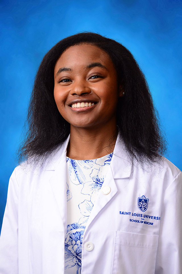 Ayanna Shambe poses for a headshot in her white coat against a blue background.