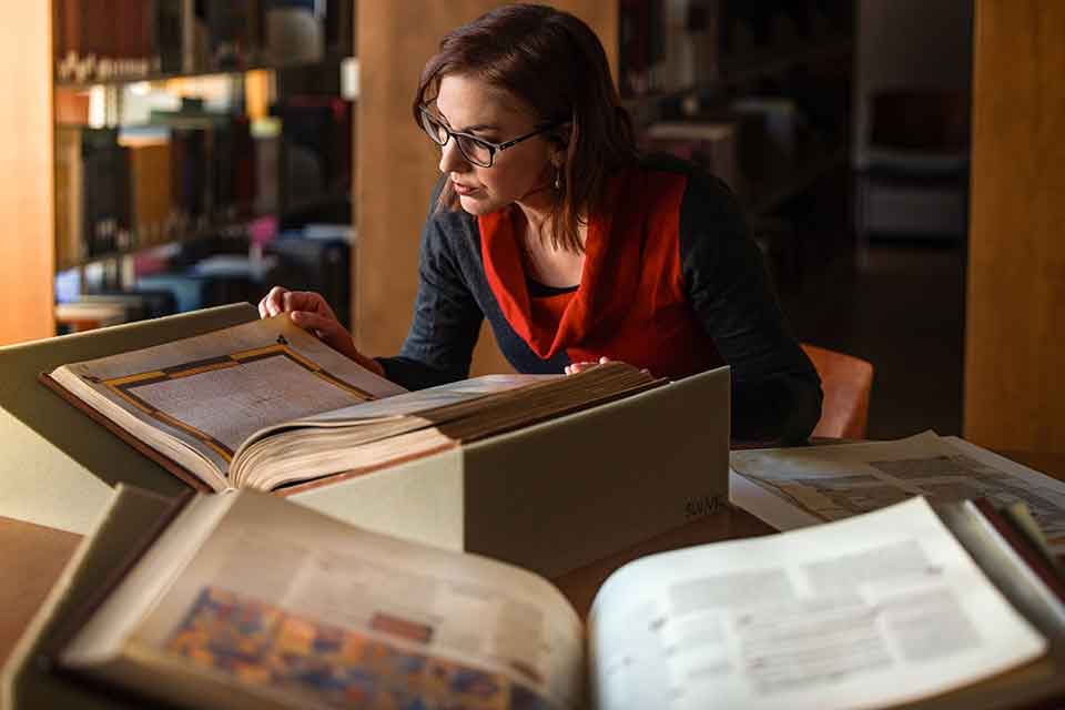 A woman examines several large manuscripts that are laid out in front of her