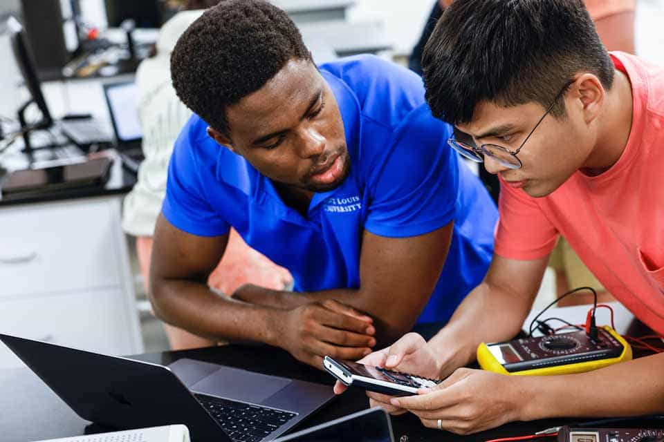 Project Lead the Way at SLU Two male students look at a calculator while working on a device in a lab.
