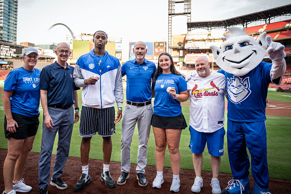 Feser with friends and the Billiken at SLU Night at the Ballpark A group of people stand with the Billiken mascot on the field at Busch Stadium